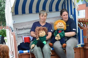 Zwei Frauen sitzen mit zwei Handpuppen in einem Strandkorb